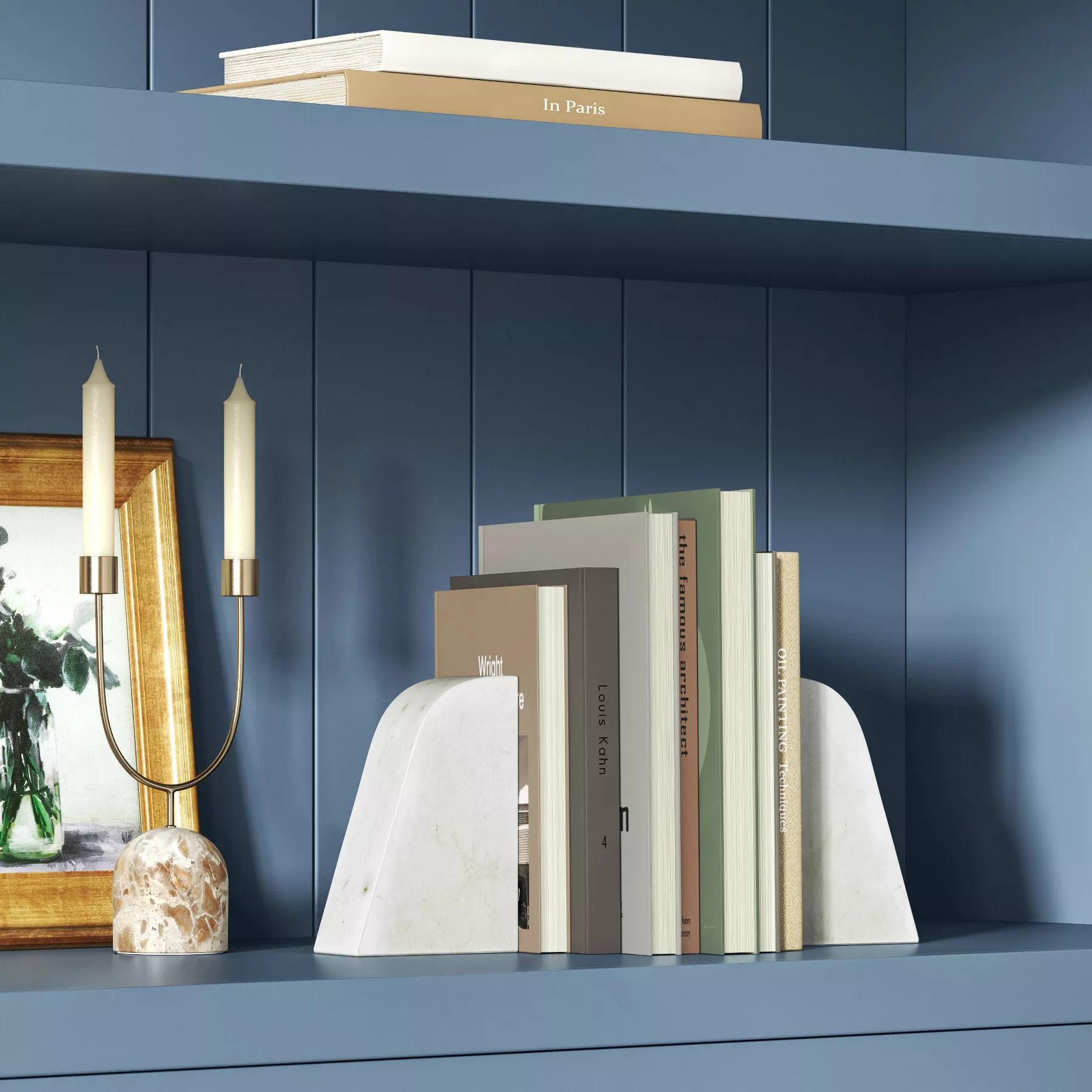 Books held upright by white marble bookends on a blue shelf. A framed photo and candle holder are beside the books