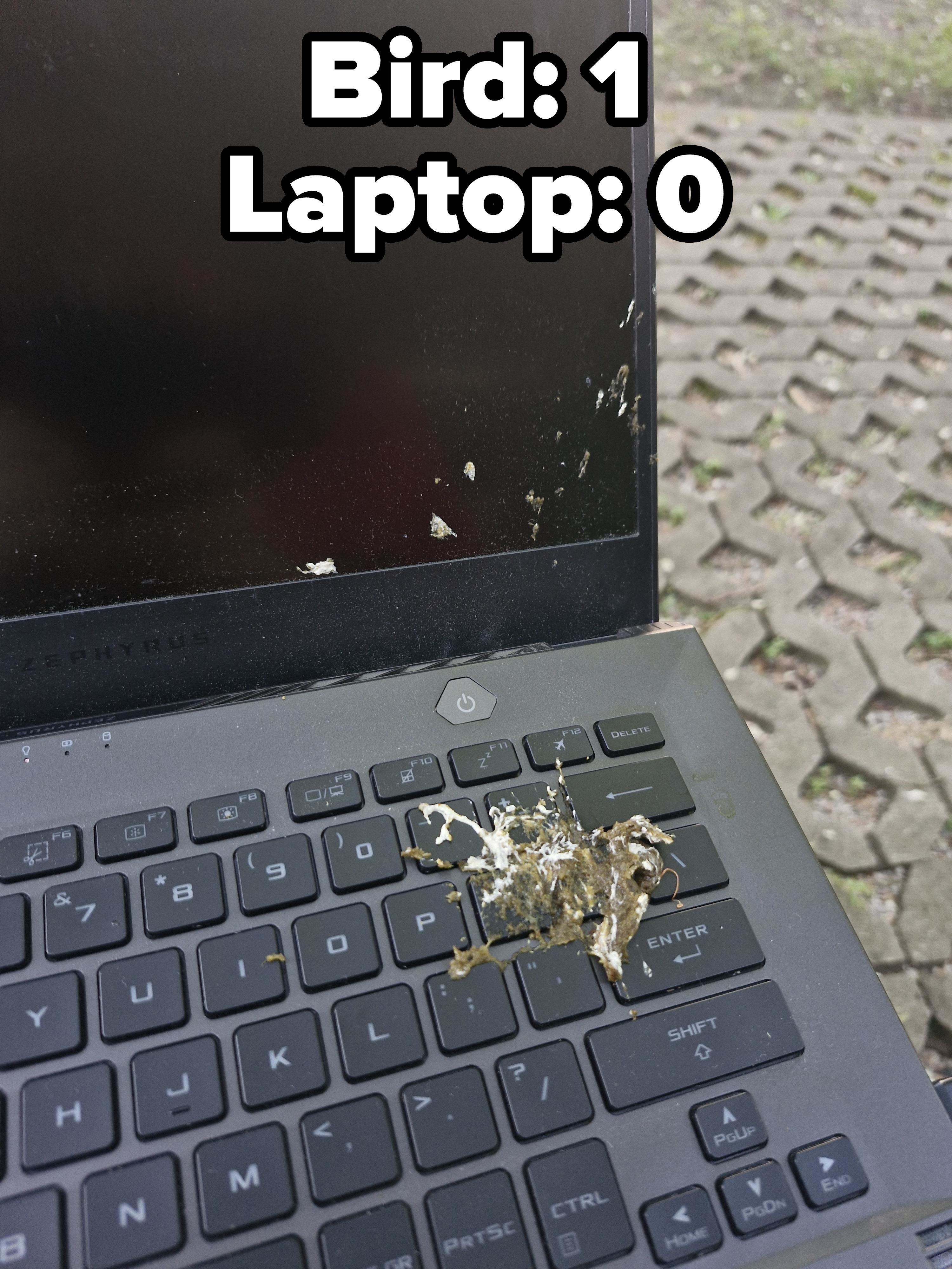 A laptop with bird droppings on the keyboard and screen, outdoors on a concrete surface
