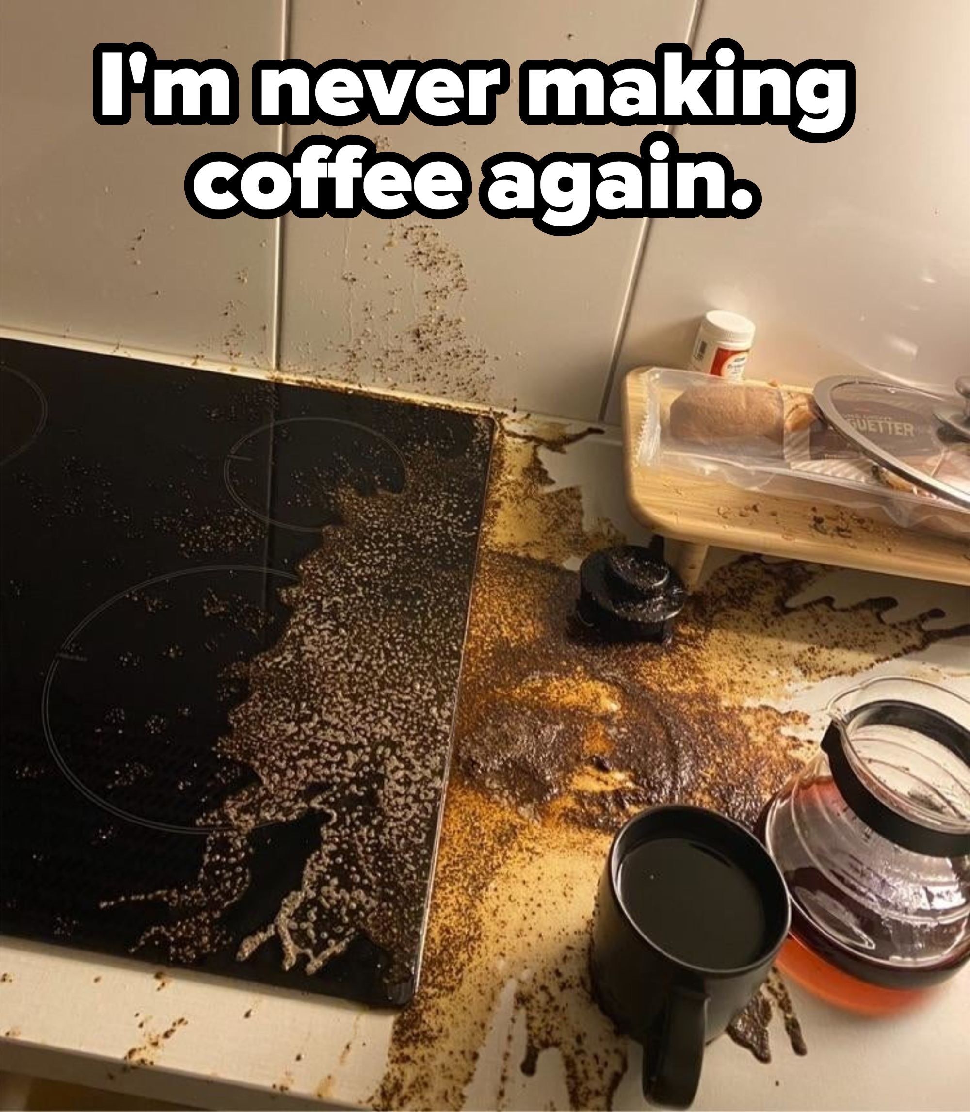 A kitchen counter with a coffee spill mess. Coffee grounds cover the stove, counter, and a black cup nearby. Coffee pot and bread loaf in the background