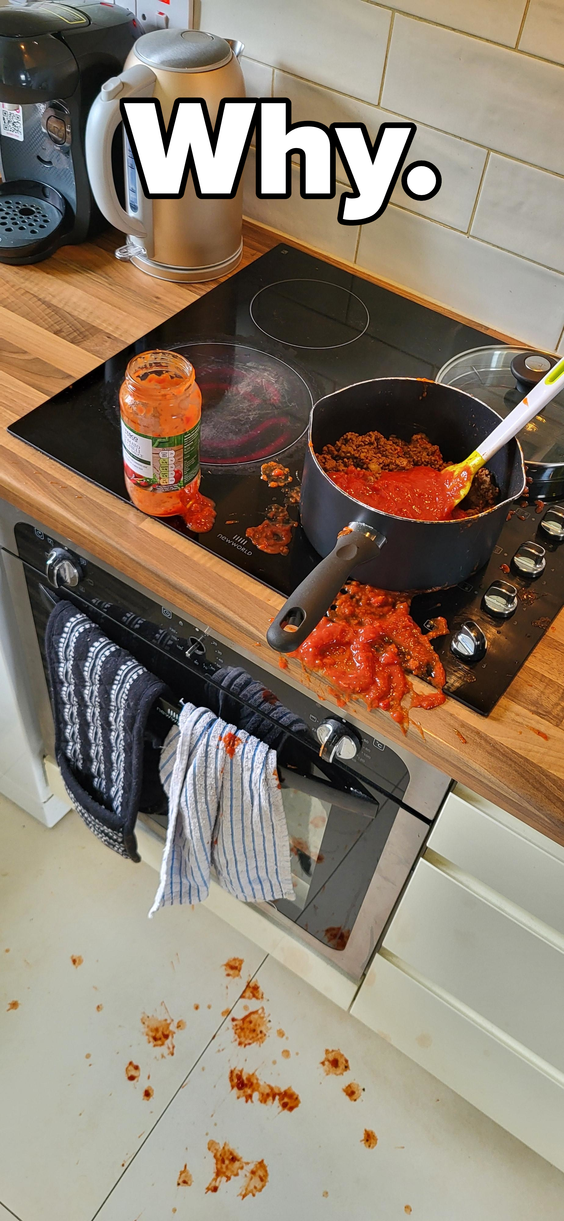 A stovetop with a pot of sauce has spilled, creating a mess on the stove and floor. A jar of sauce is open beside the pot. Towels hang from the oven door