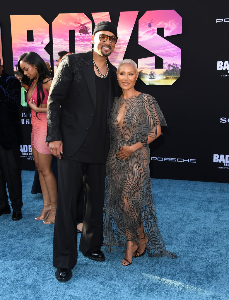 Will Smith in a black suit and Jada Pinkett Smith in a sheer, geometric-patterned dress pose together on the red carpet at the "Bad Boys" premiere