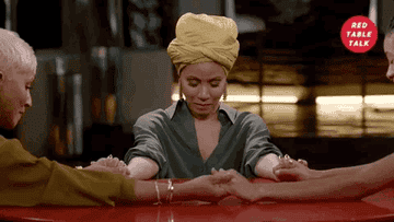 Jada Pinkett Smith, wearing a yellow turban and green shirt, holds hands with Adrienne Banfield-Norris and Willow Smith, who are off-frame, on "Red Table Talk."