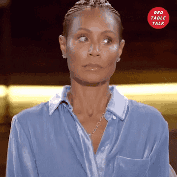 Jada Pinkett Smith looks to the side with a surprised expression during an episode of "Red Table Talk." She is wearing a light-colored blouse