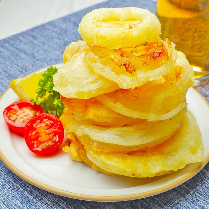 お皿に積み重ねられたオニオンリング、トマトのスライスとレモンのくし形切りも添えられています。