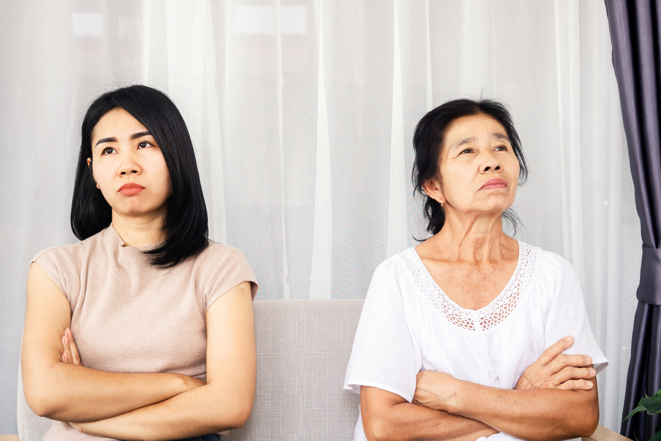 Two women sit with arms crossed, both looking pensive and upset, suggesting a disagreement or conflict