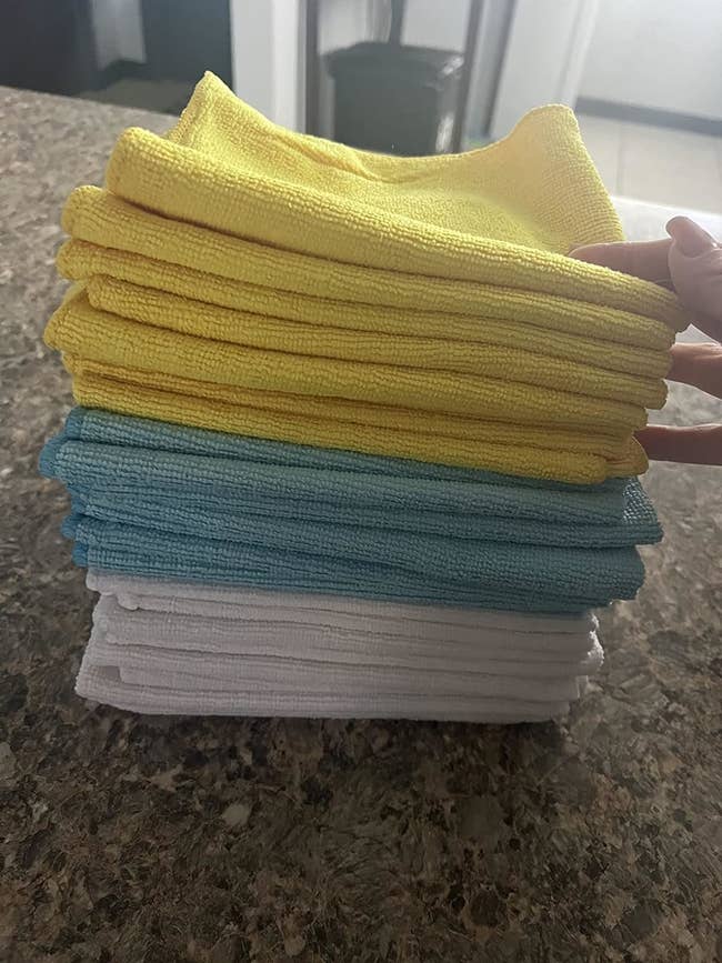 Stack of neatly folded towels successful yellow, blue, and achromatic colors connected a countertop. The manus of a idiosyncratic is adjusting the apical towel