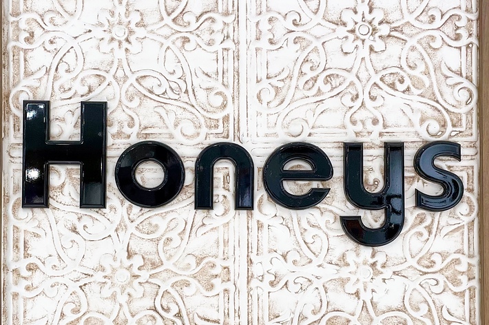 装飾的なバックグラウンドの前に「Honeys」のロゴ。