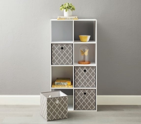 White cube storage organizer with four patterned fabric bins, two empty shelves, and a small potted plant on top