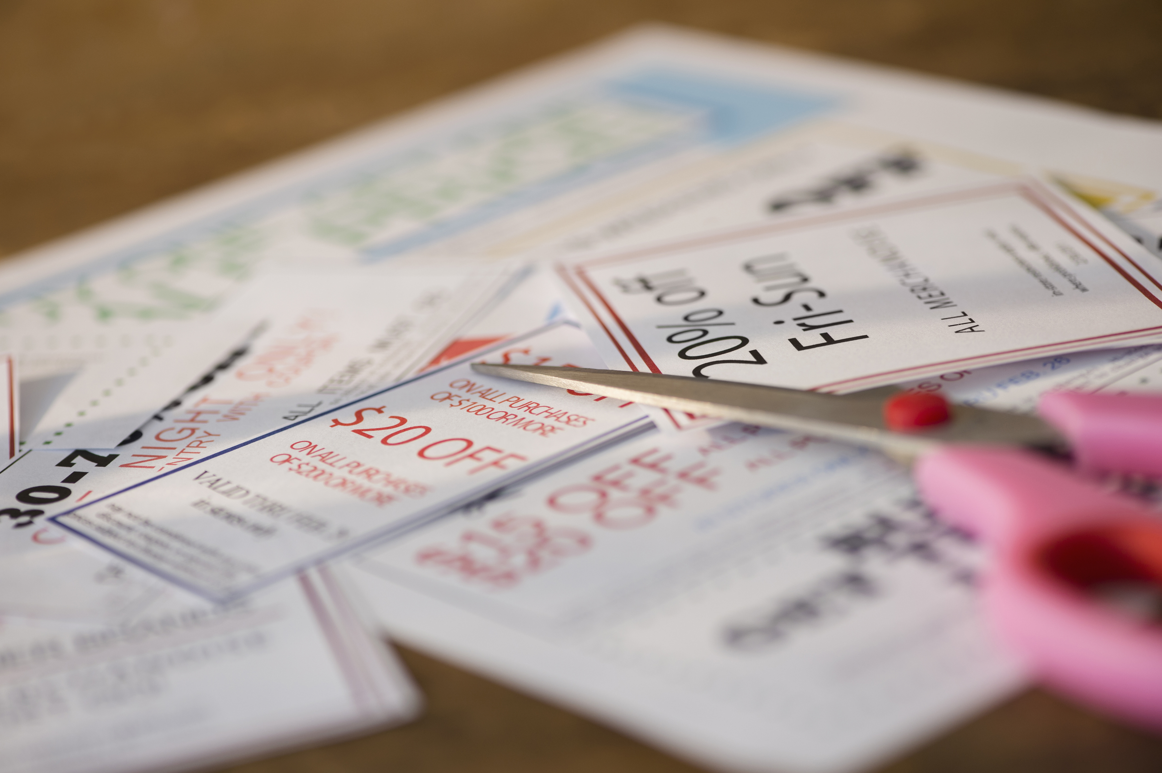 Scissors cut out paper coupons, offering various discounts such as &quot;20% off&quot; and &quot;$20 off,&quot; highlighting savings strategies