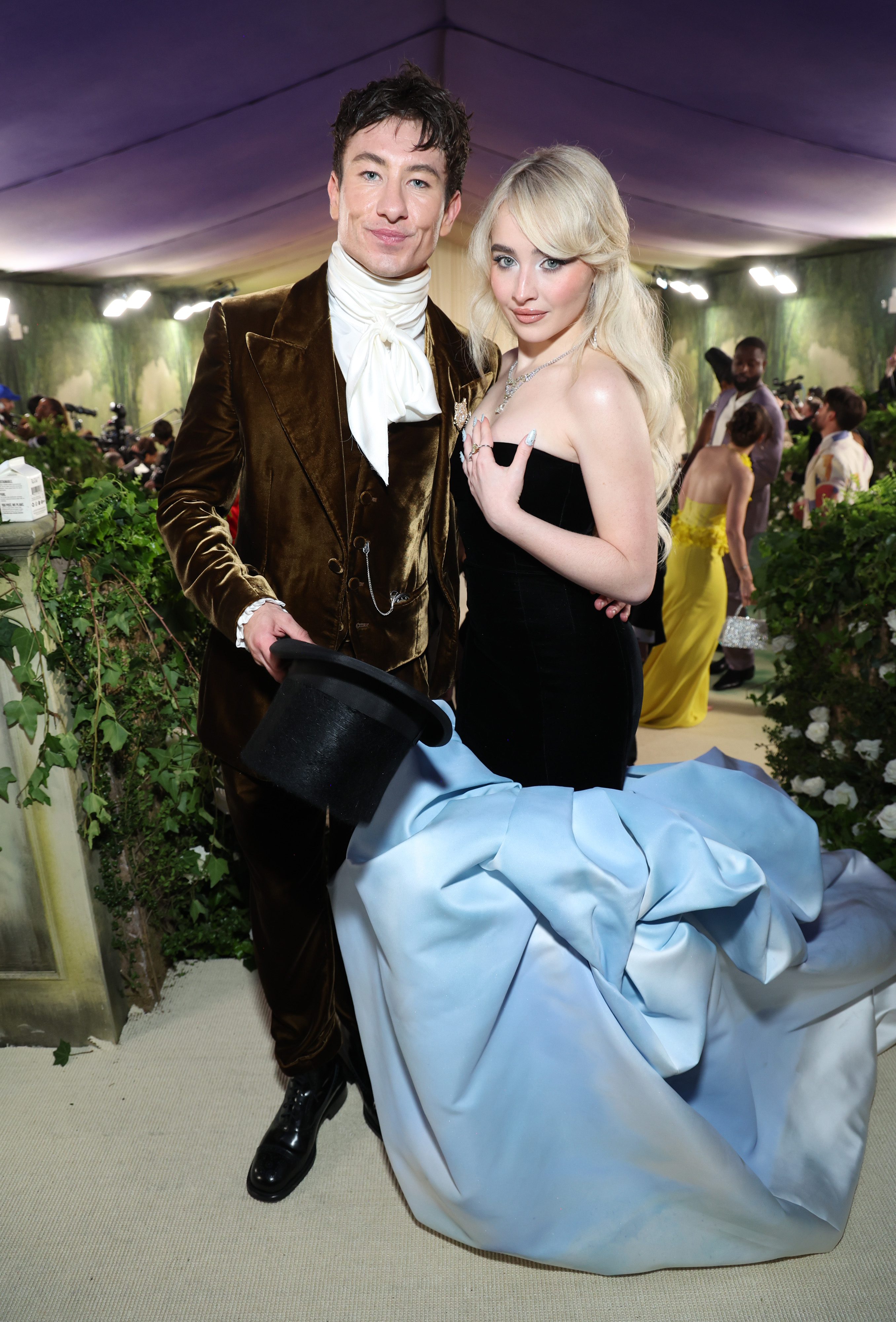 Barry Keoghan in a vintage-inspired suit and Sabrina Carpenter in a strapless black dress with a blue train, posing together at an event