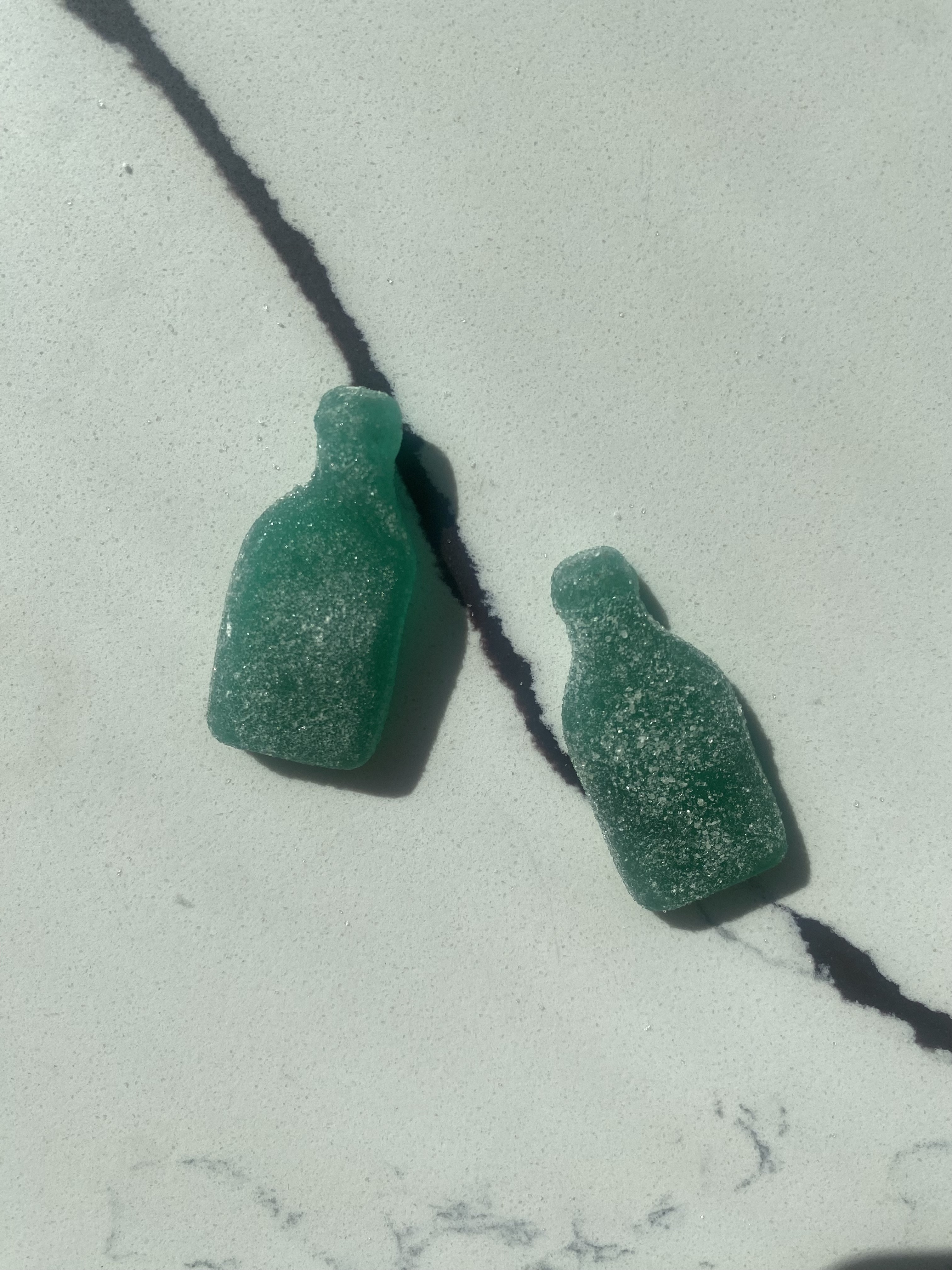 Two blue bottle-shaped gummy candies with a sugar coating rest on a marble surface
