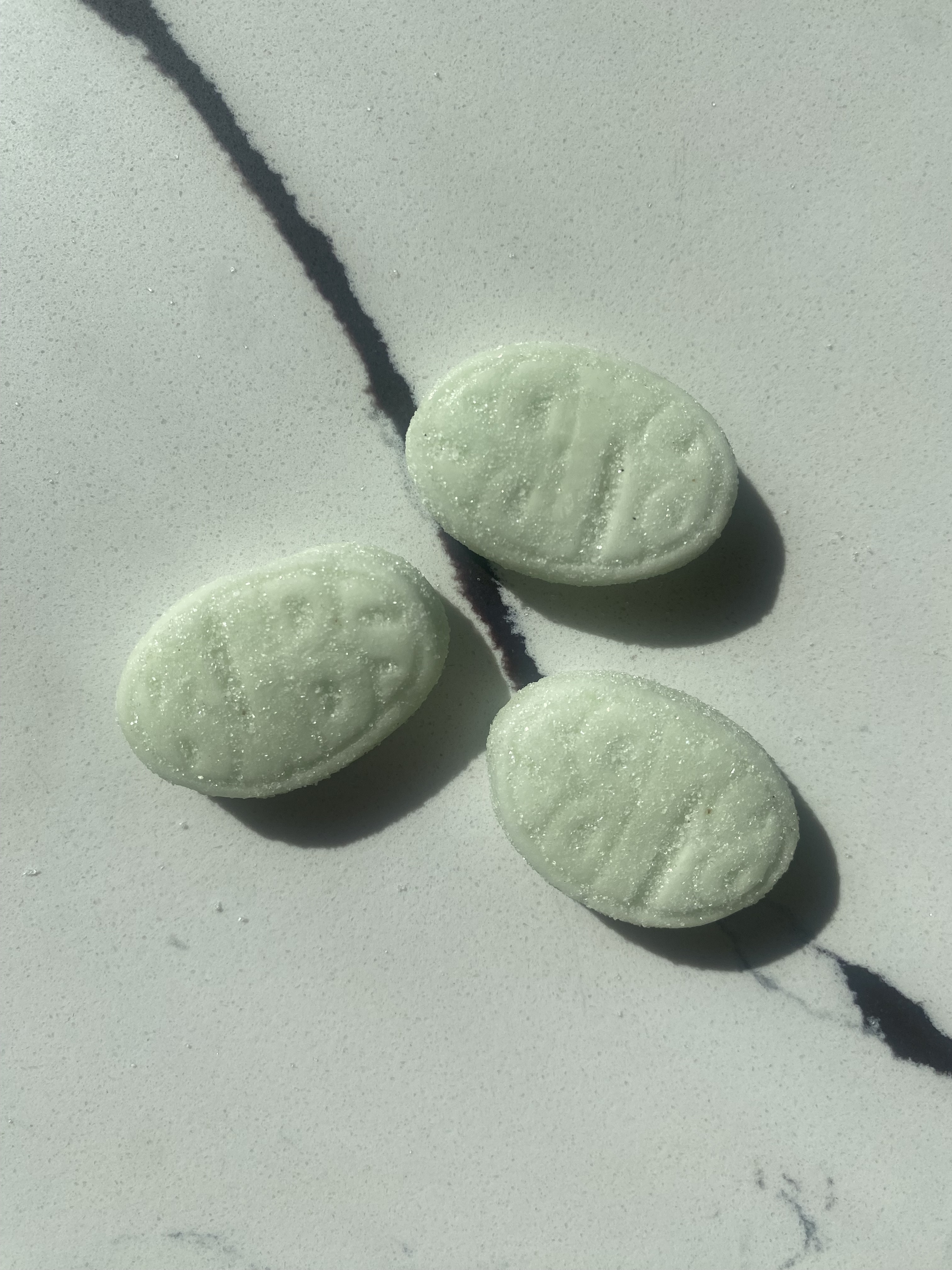 Three oval-shaped green gummy candies with embossed &quot;Bubs&quot; text, placed on a marble surface