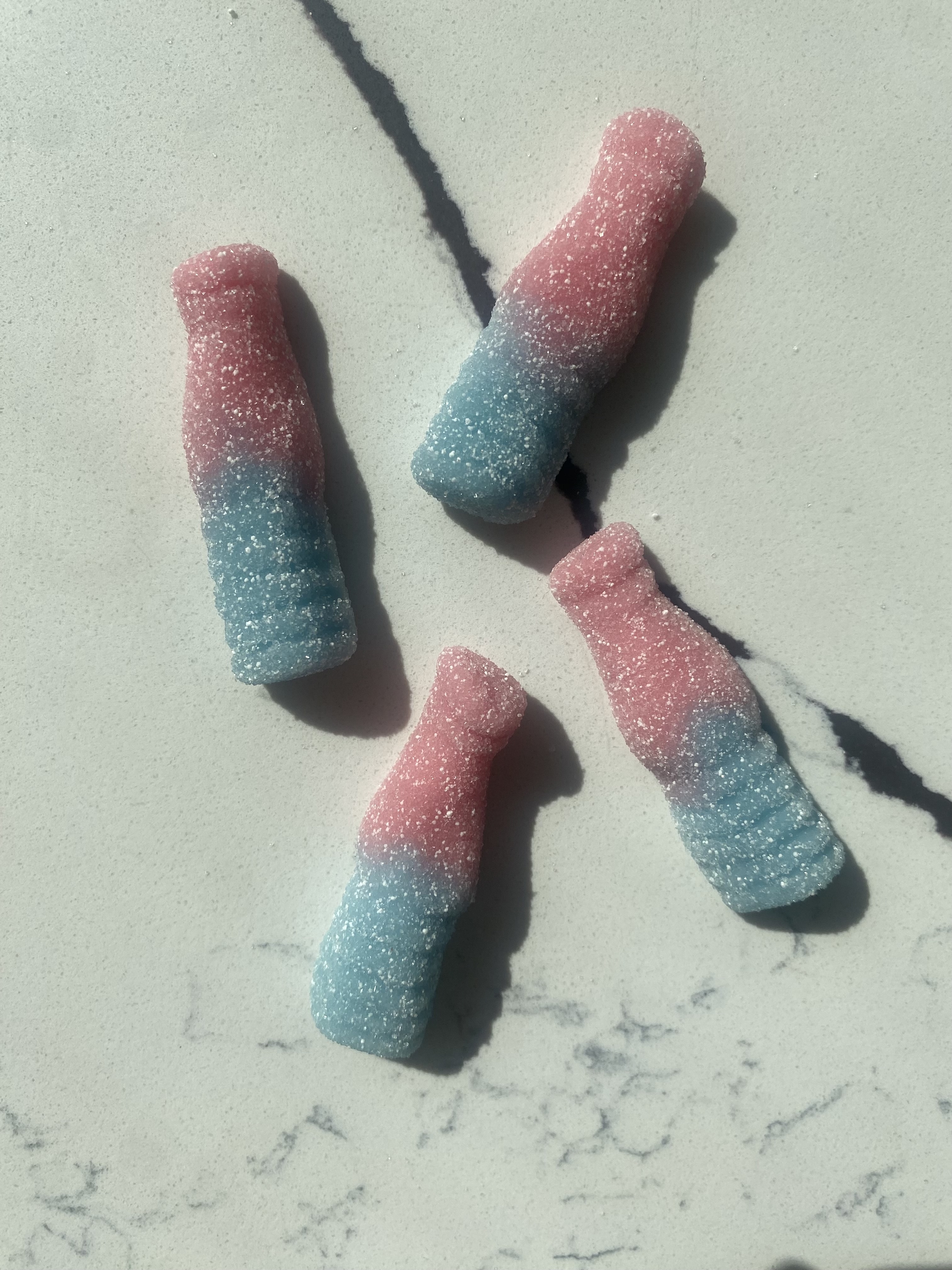 Four gummy blue and pink cola bottle candies with a sugary coating lie on a marble surface