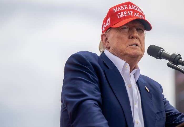 Donald Trump speaks at a podium wearing a "Make America Great Again" hat