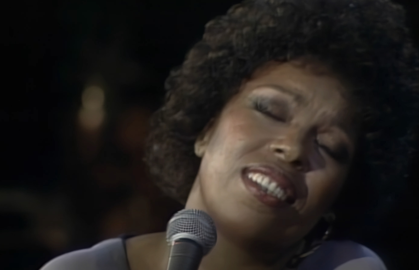 A singer passionately performing on stage with eyes closed, holding a microphone close to her mouth