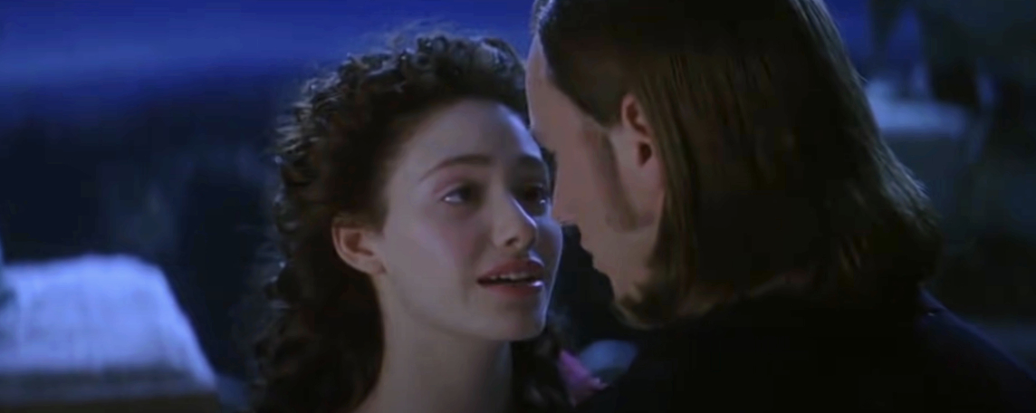 Emmy Rossum and Patrick Wilson in a close-up scene from the musical film "The Phantom of the Opera," with Emmy looking emotional