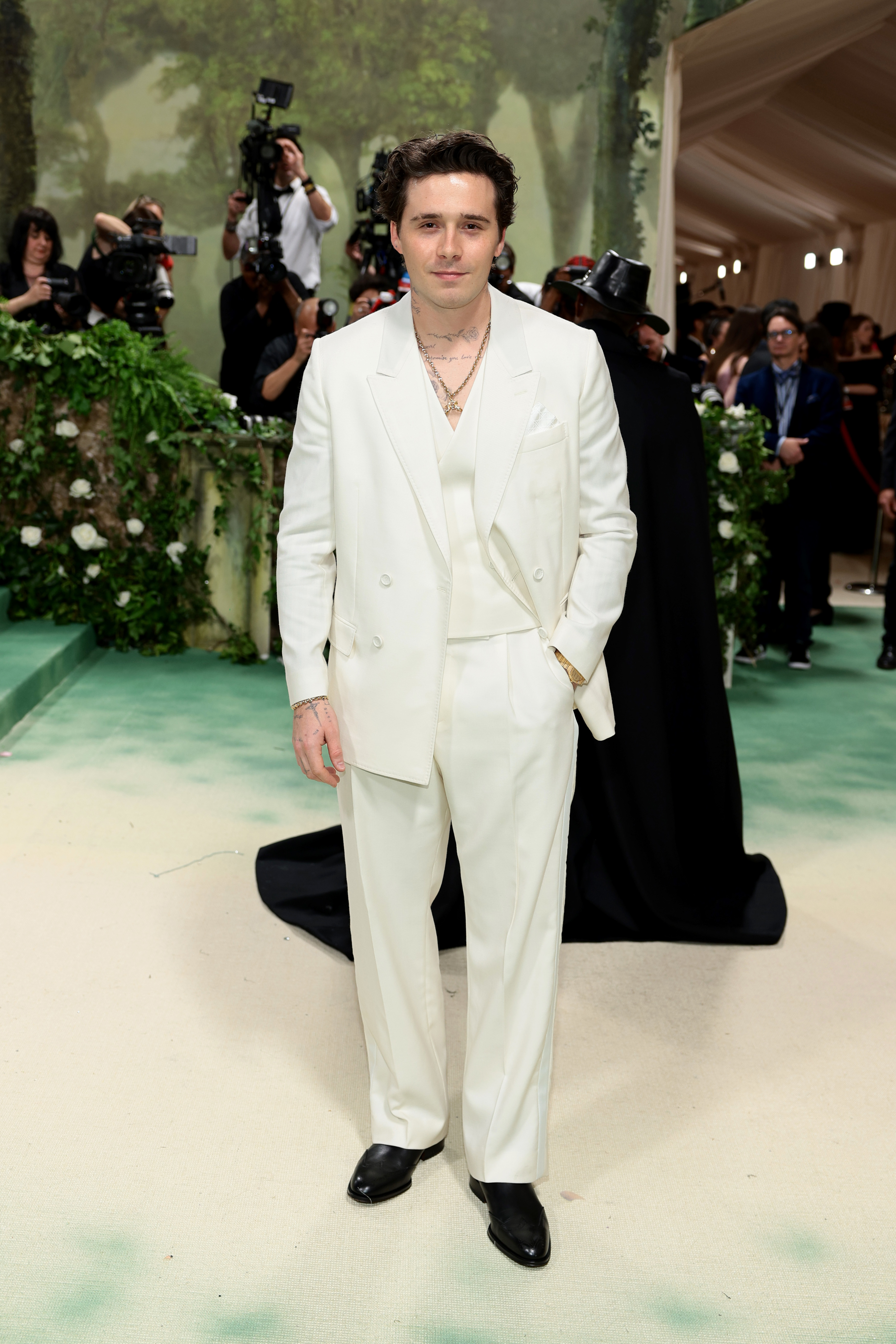 Brooklyn Beckham on the red carpet wearing a sleek, light suit, surrounded by photographers
