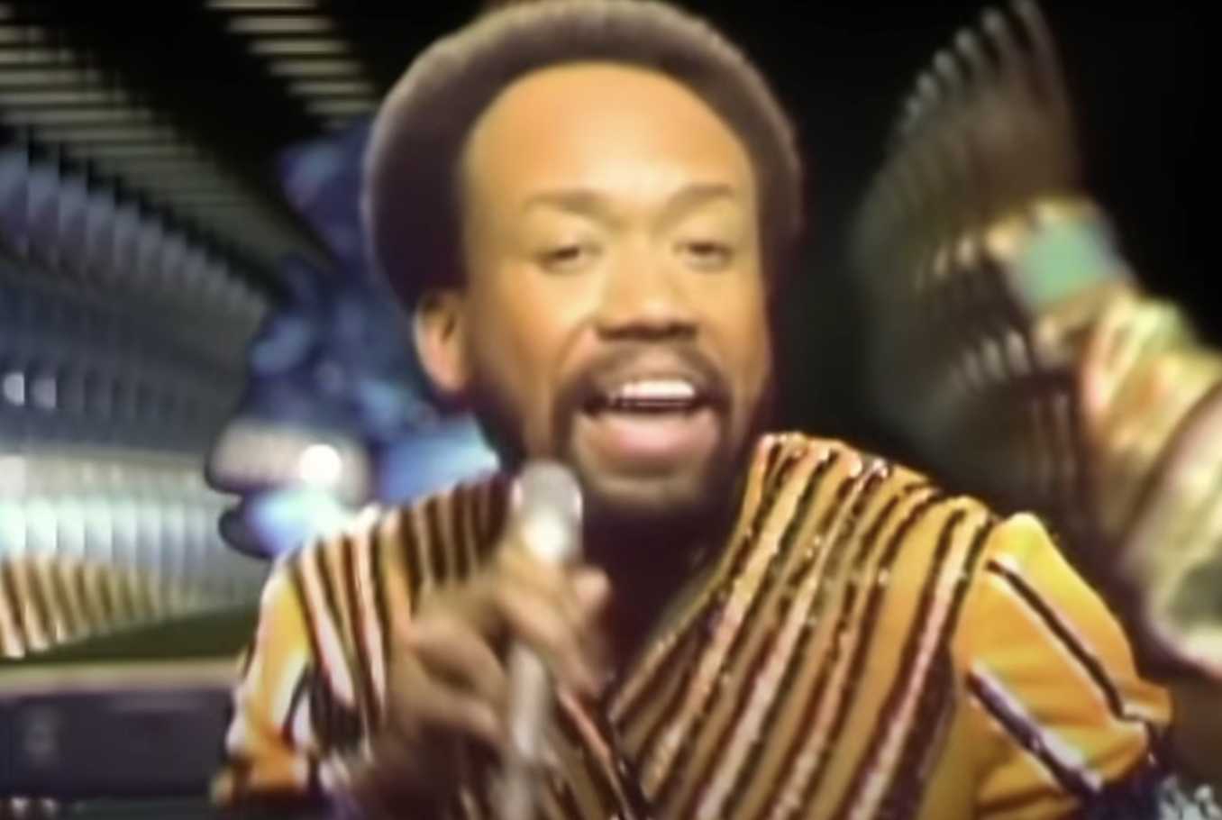 Maurice White of Earth, Wind & Fire performs energetically, wearing a striped outfit