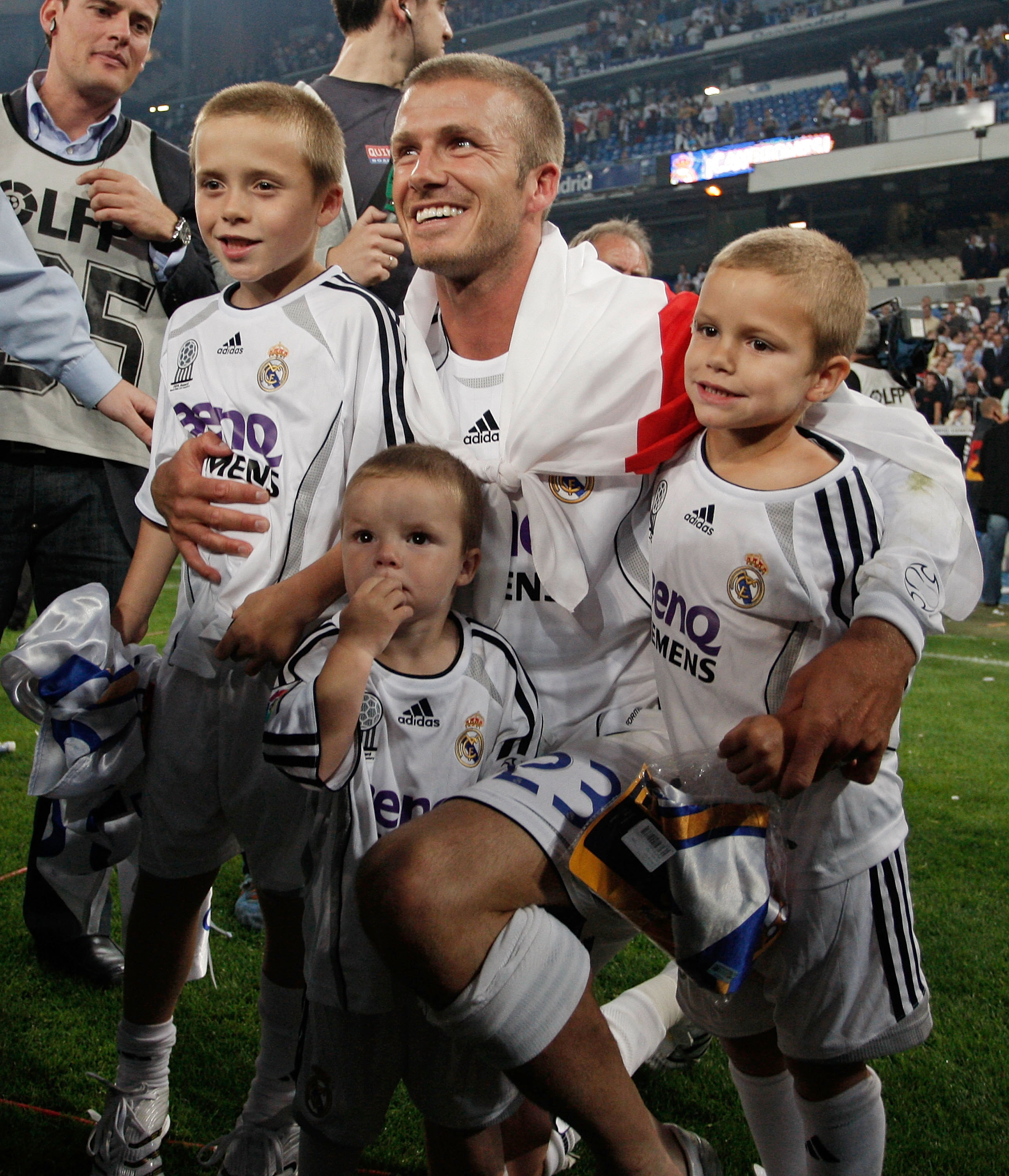 David Beckham, in a Real Madrid jersey, poses with his three children who are also in Real Madrid jerseys, on a football field