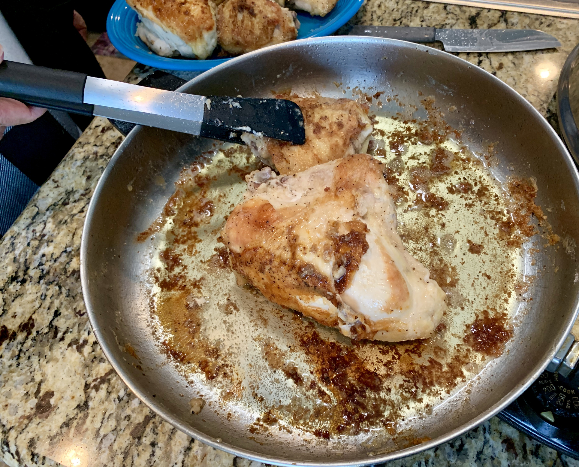 Two chicken breasts being cooked in a frying pan. One piece is being handled with tongs