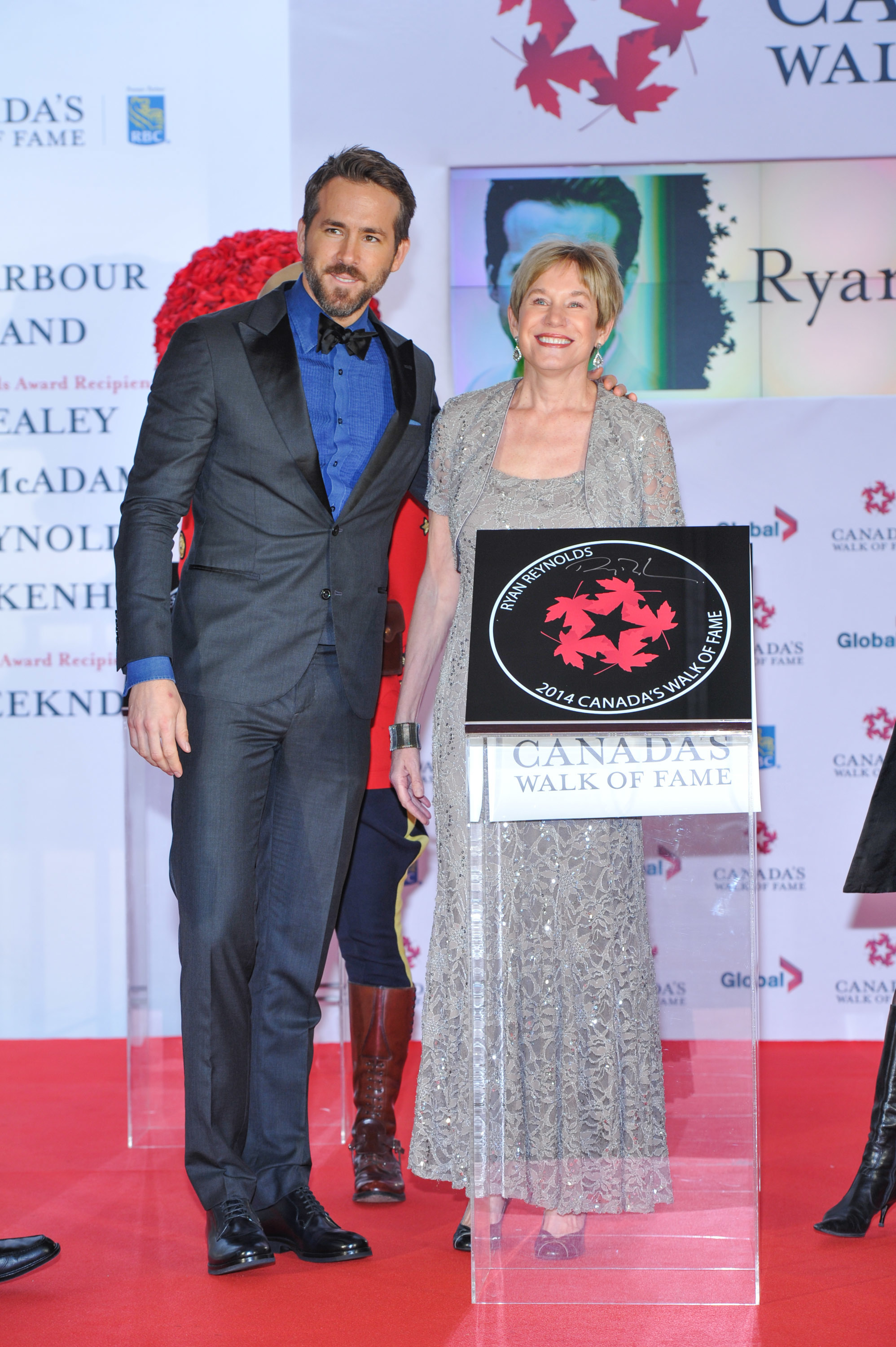 Ryan Reynolds and another person smile and pose on the red carpet at Canada's Walk of Fame event. Ryan is in a suit, while the other person is in an elegant gown