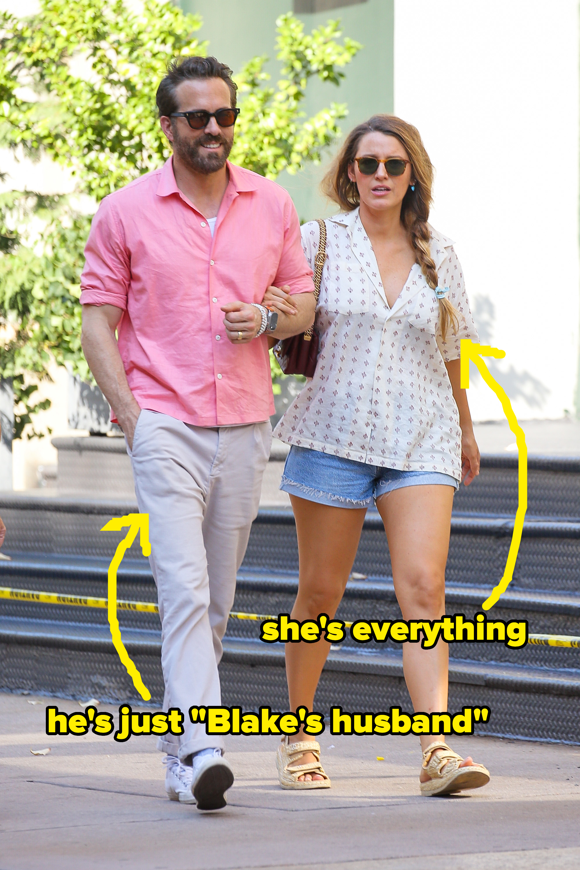Ryan Reynolds in a casual pink shirt and khaki pants, walking with Blake Lively in a white patterned top and denim shorts, both wearing sunglasses