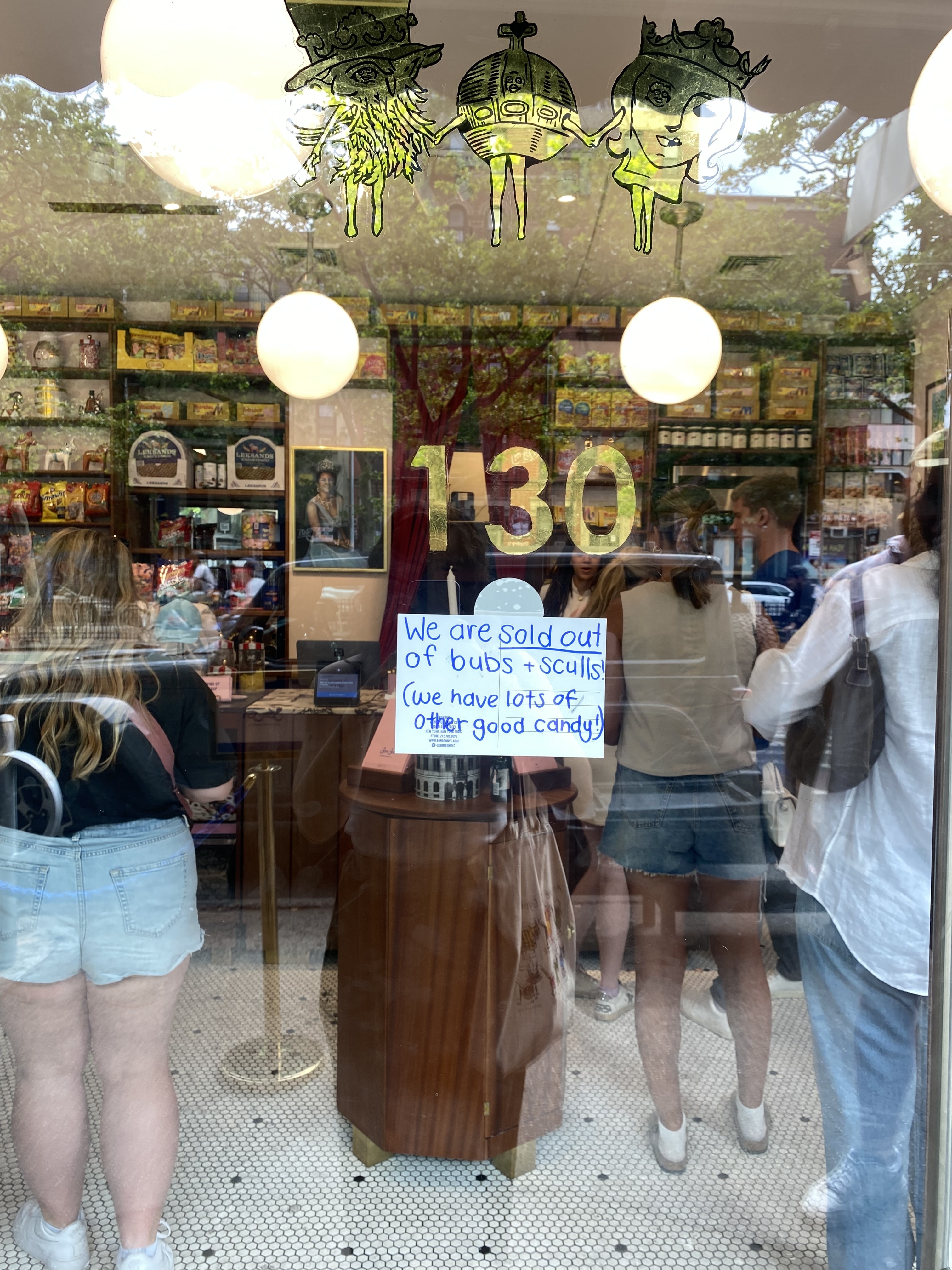A store window displays a sign reading, &quot;We are sold out of bubs + sculls (we have lots of other good candy),&quot; with people inside shopping