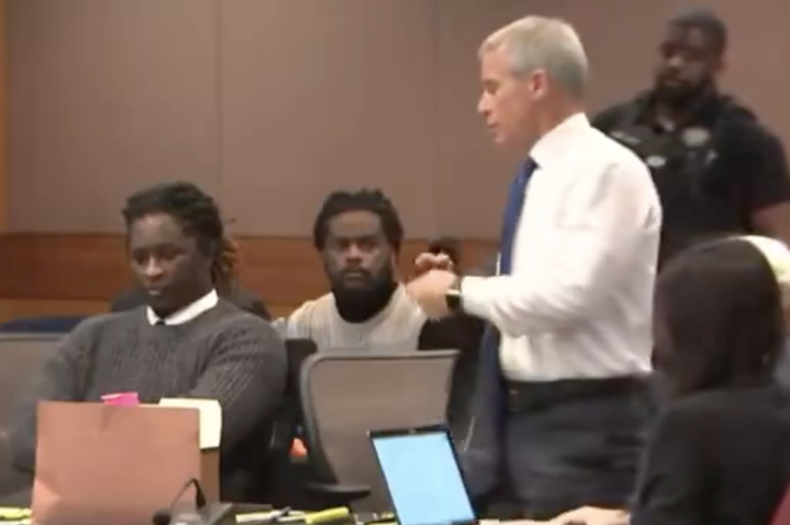 Young Thug appears in a courtroom with his lawyer and an officer. Another individual sits behind them