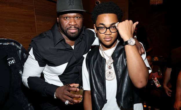 50 Cent and Michael Rainey Jr. pose together at an event. 50 Cent wears a black and white shirt with a cap, while Michael sports a vest over a white T-shirt and glasses