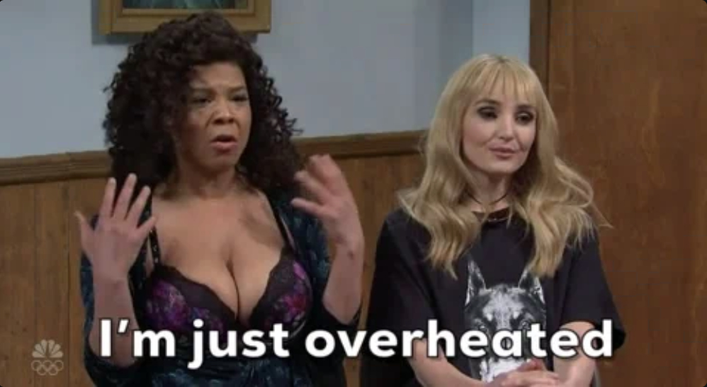 Two women in conversation from an NBC sketch; one expresses being overheated using hand gestures, and subtitles show &quot;I'm just overheated.&quot;
