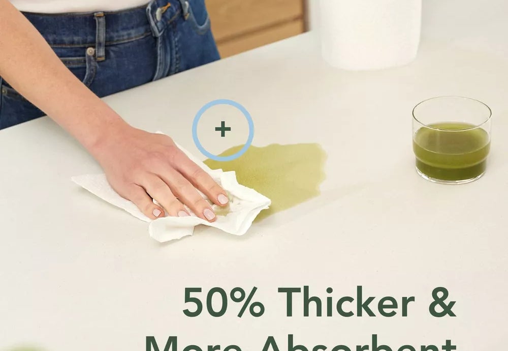 A person cleans a green liquid spill on a countertop using a paper towel next to the text: &quot;50% Thicker &amp;amp; More Absorbent&quot;