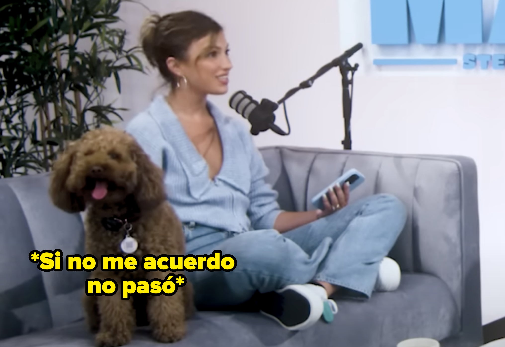 Mujer sentada en un sofá con un perro a su lado, sosteniendo un teléfono, hablando en un micrófono durante una grabación