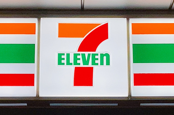 セブンイレブンの看板が店内の照明の上に表示されています。下には「新 あったか麺 さらにコシ強く、つゆ香る」と書かれています。