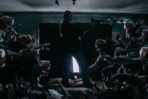 Person stands ready to fight numerous monstrous creatures in a dark room, with a light source behind them casting shadows and creating an intense atmosphere