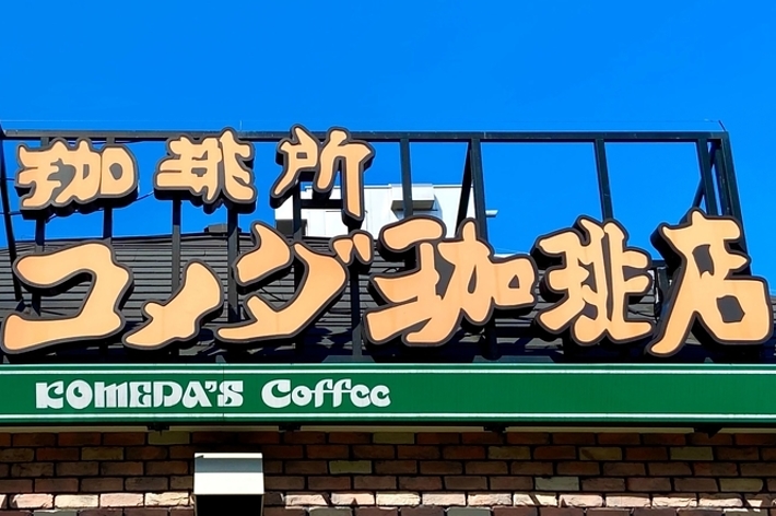 Sign for Komeda&rsquo;s Coffee on top of a brick building with a clear sky background. The sign features both Japanese characters and the cafe&rsquo;s name in English