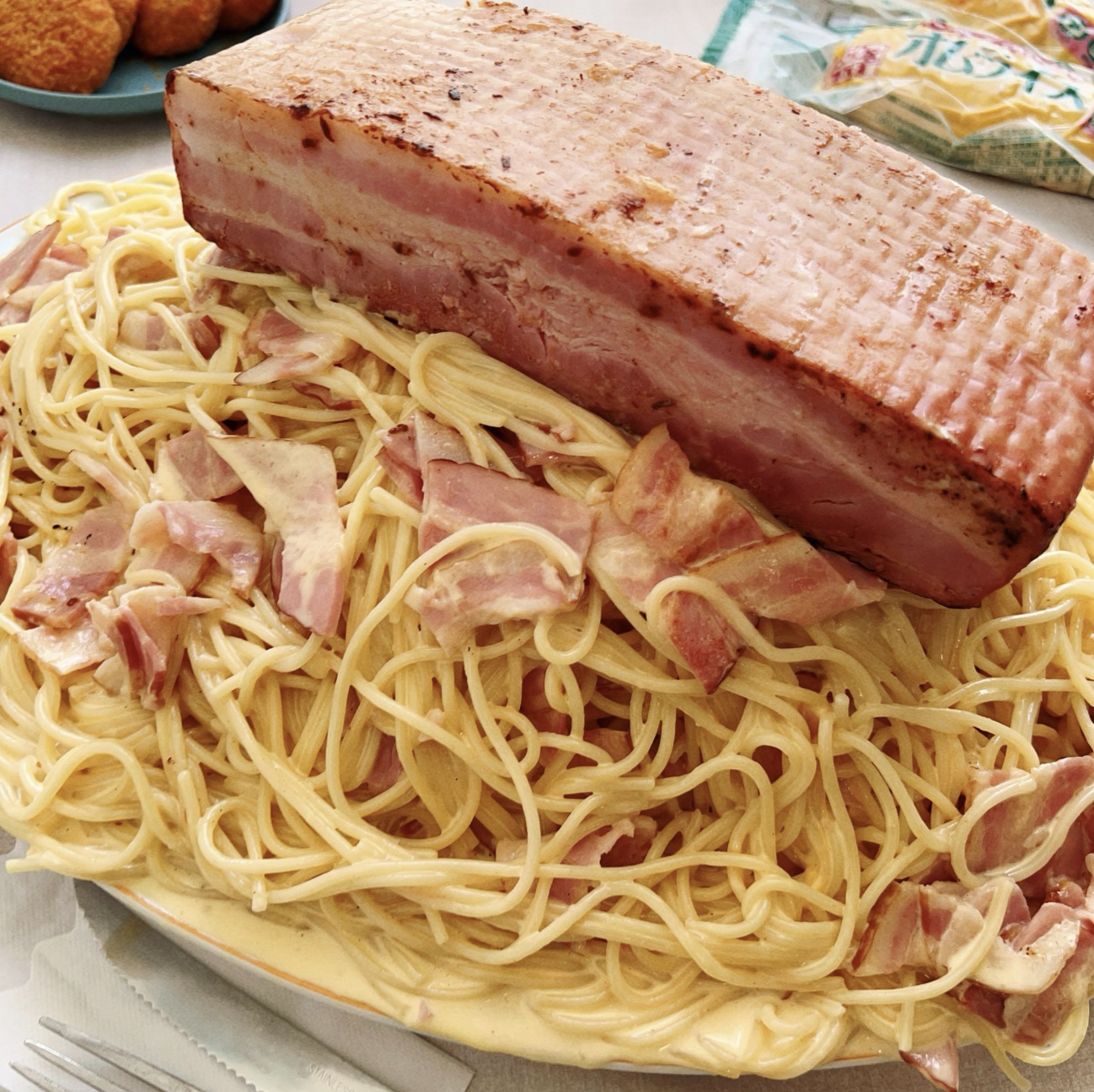 スパゲッティの上に大きなベーコンのブロックが乗っている料理の画像。