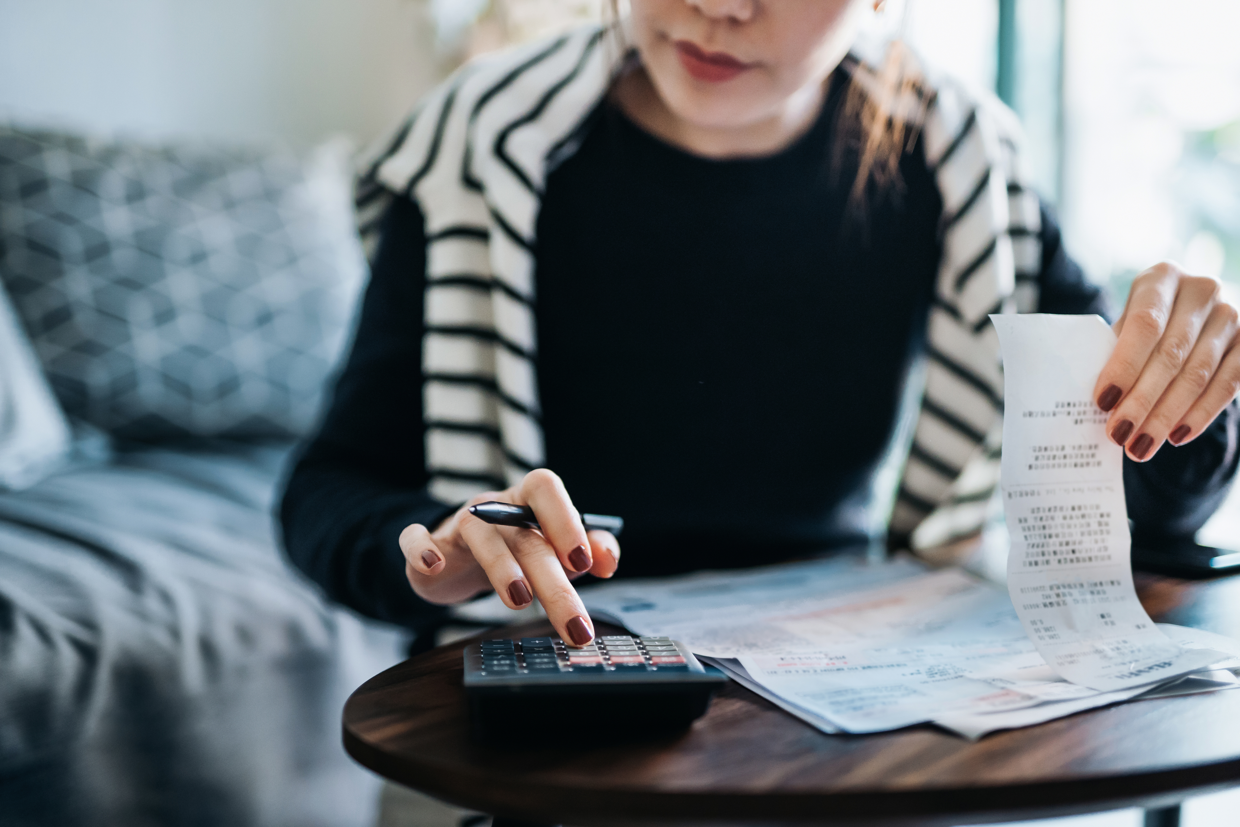A woman reviews receipts and documents while calculating expenses on a calculator at a table in a home setting