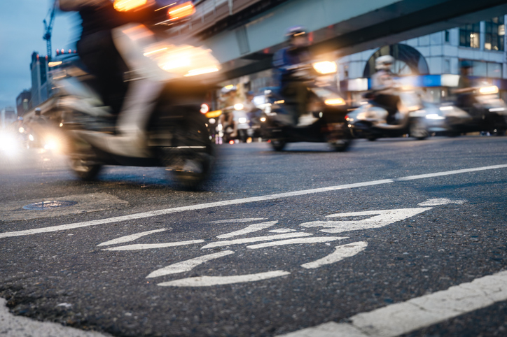 Busy city street with blurred motorcycles passing by and a bicycle lane marking on the road