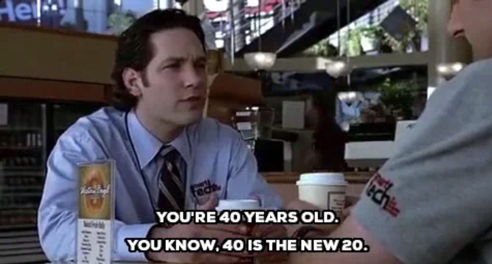 Paul Rudd converses with a man in a shirt and tie at a coffee shop. Text on the image reads: &quot;You're 40 years old. You know, 40 is the new 20.&quot;