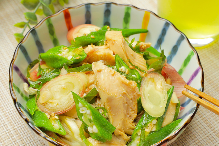 鶏肉とオクラがたっぷり入った和風サラダ。横には飲み物が置かれている。緑の葉が背景にあります。