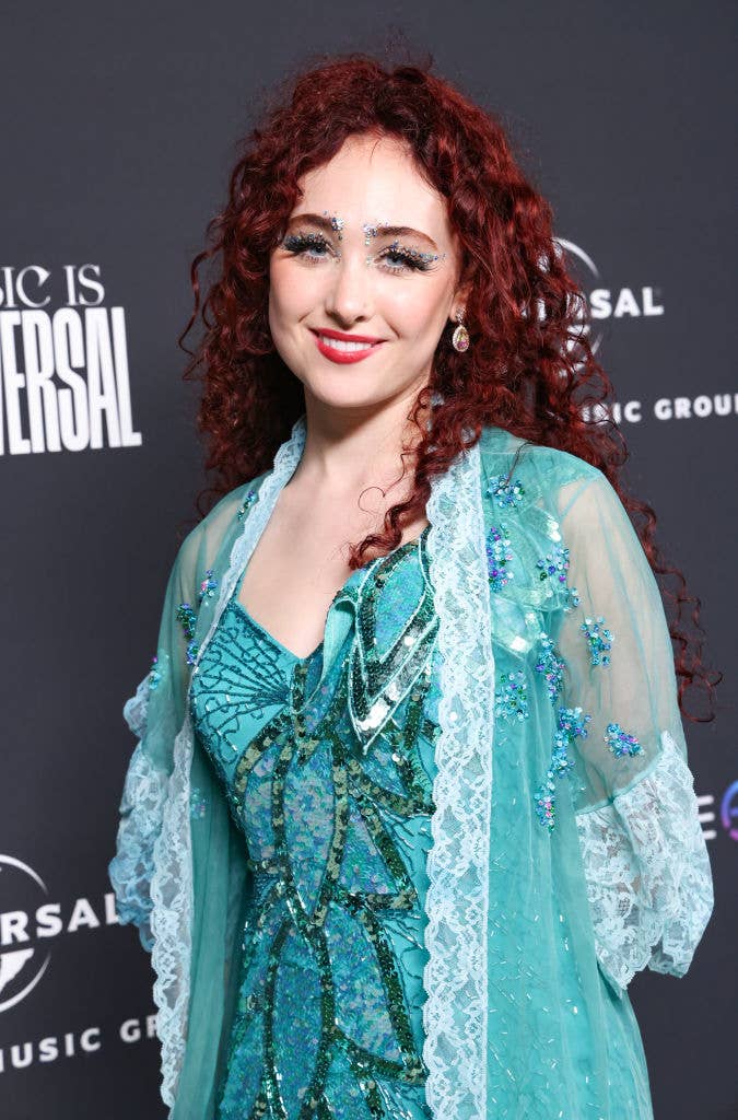 I don't know who this is. Person with red curly hair in an elaborate teal outfit with lace and beaded details, posing at a Universal Music Group event