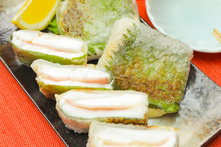 日本料理の皿に、白身魚と大葉を挟んだ天ぷらが盛られている。付け合わせにレモンとおろしポン酢が添えられている。