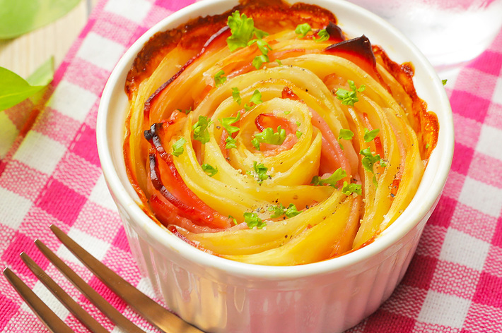 きれいに盛り付けられた野菜のローストが白い器に入っている。隣にフォークが置かれ、背景にチェック柄の布が敷かれている。