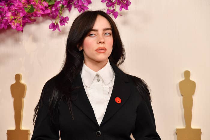 Billie Eilish, wearing a blazer over a shirt, stands with a serious expression
