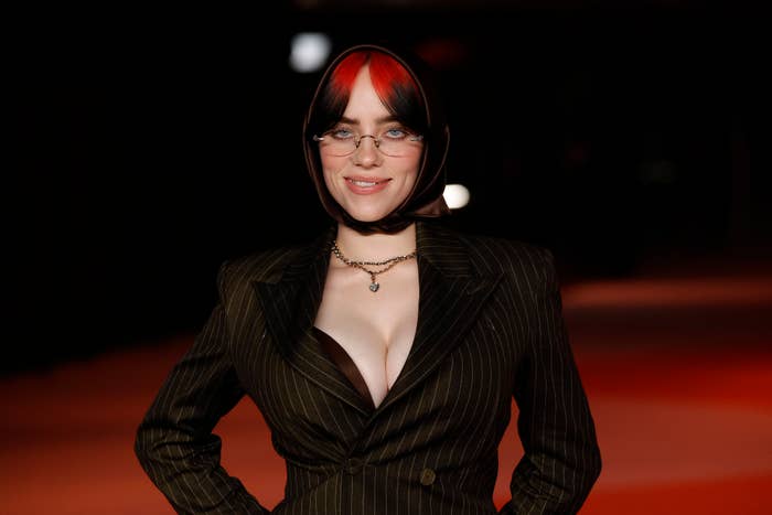 Billie Eilish on the red carpet wearing a pinstriped suit with a headscarf and glasses, accessorized with a necklace