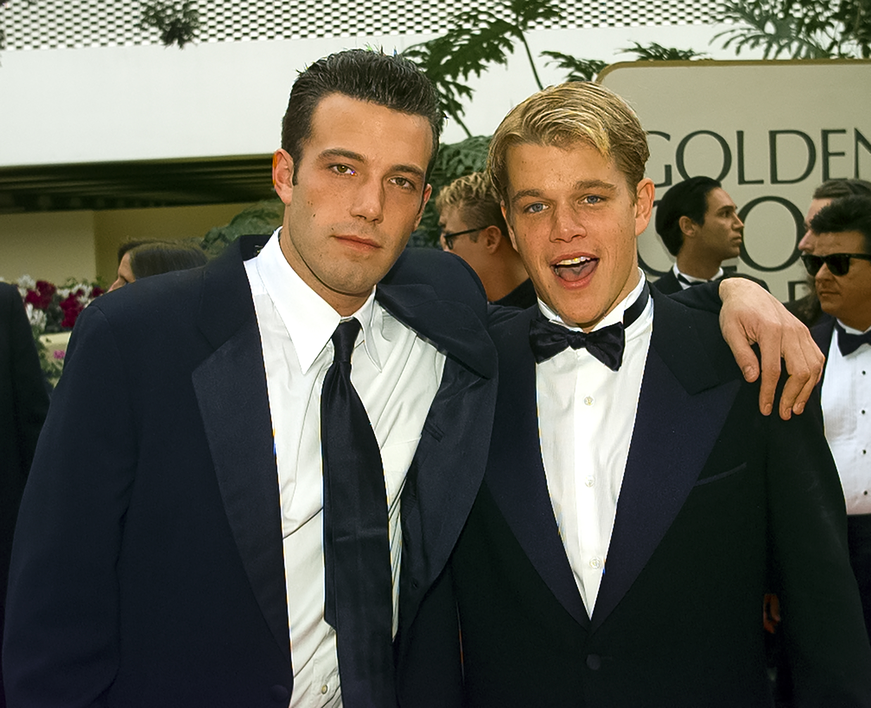 Ben Affleck and Matt Damon when they were younger at the Golden Globe Awards, both wearing tuxedos and smiling with arms around each other