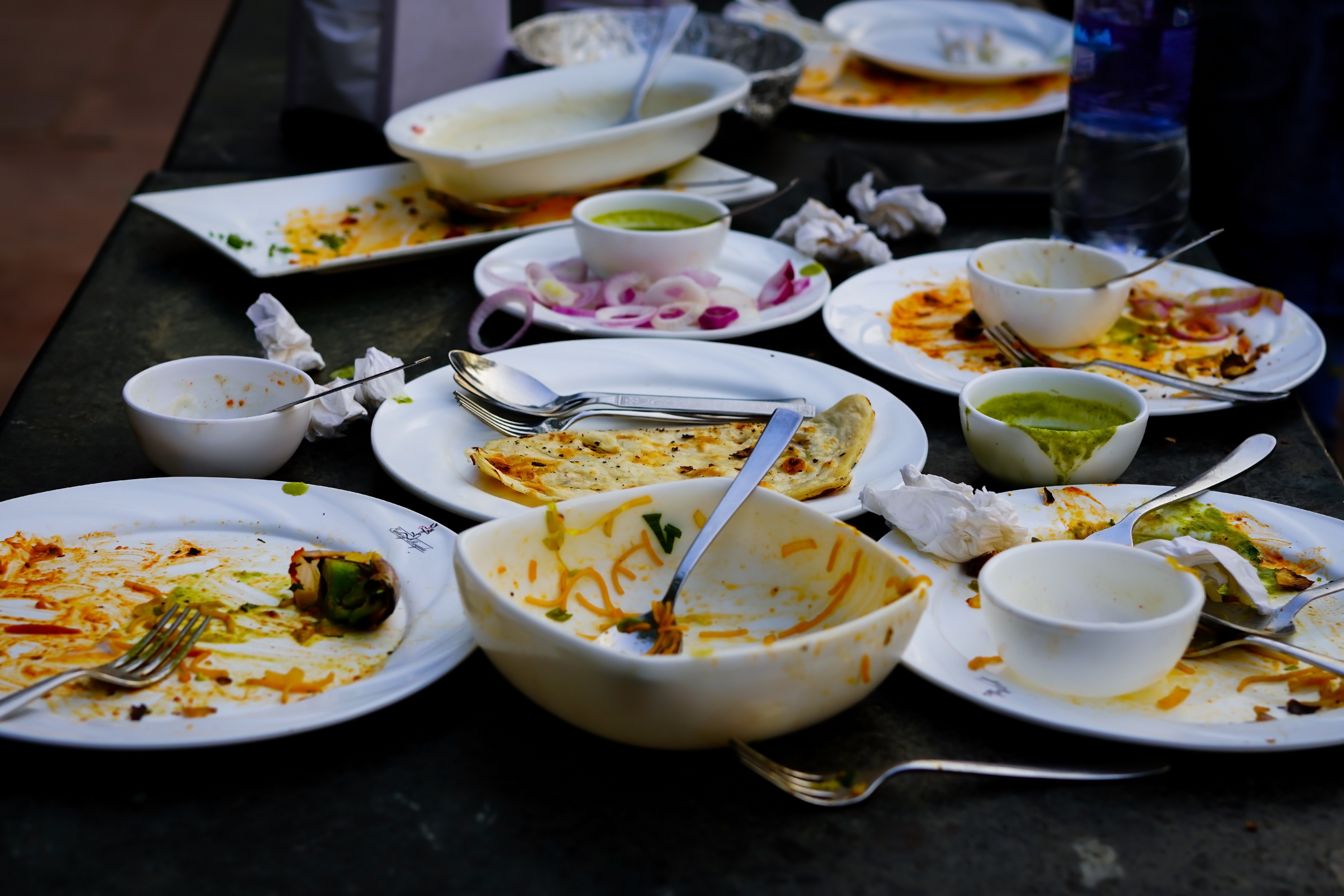 A table filled with empty dishes, plates, and bowls, with leftover food scraps and used utensils, indicating a recently finished meal