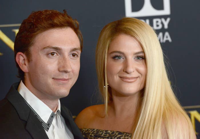 Daryl Sabara and Meghan Trainor pose together on a red carpet. Daryl wears a suit jacket. Meghan has long hair styled straight and wears an off-the-shoulder dress