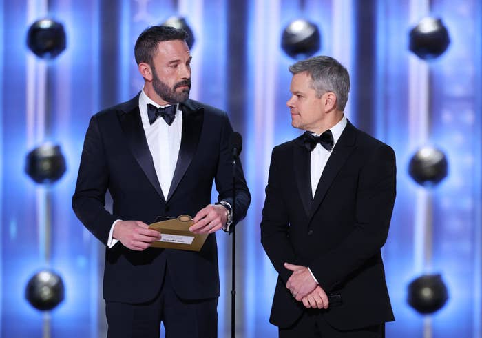 Ben Affleck and Matt Damon stand on stage in suit and present an award
