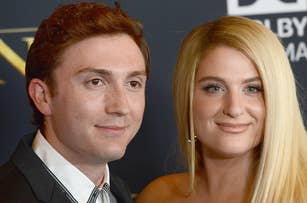 Two people, Daryl Sabara and Meghan Trainor, pose together on a red carpet. Daryl wears a suit jacket. Meghan has long hair styled straight and wears an off-the-shoulder dress